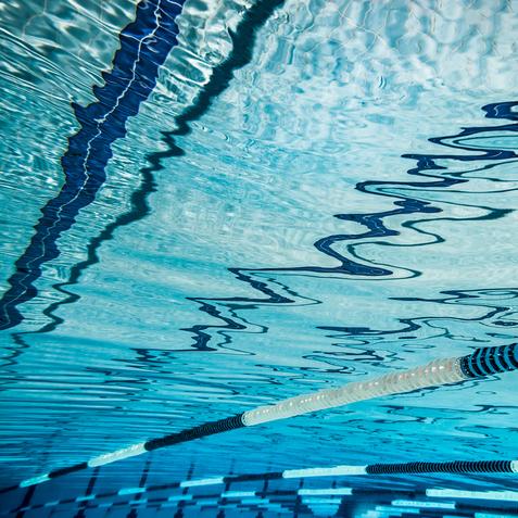 Unterwasseraufnahme eines Schwimmbeckens mit reflektierender Wasseroberfläche und Markierungen auf dem Boden.