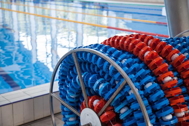 Ein rollbarer Ständer mit blauen und roten Schwimmleinen steht neben einem Schwimmbecken mit reflektierender Wasseroberfläche.