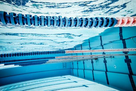Unterwasseraufnahme eines Schwimmbeckens mit blauen und roten Schwimmbahnmarkierungen sowie klarer Wasseroberfläche.
