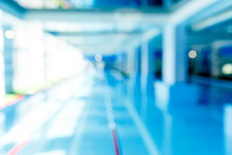 Unscharfes Bild eines modernen Schwimmbeckens mit blauer Wasseroberfläche und hellem, lichtdurchflutetem Raum.